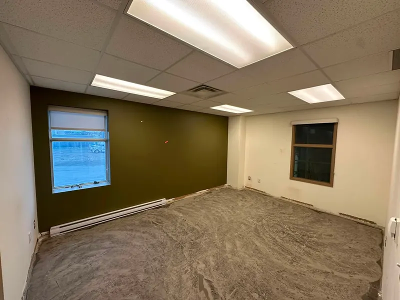 Office room with an olive green accent wall, white walls and a drop ceiling, floor still bare